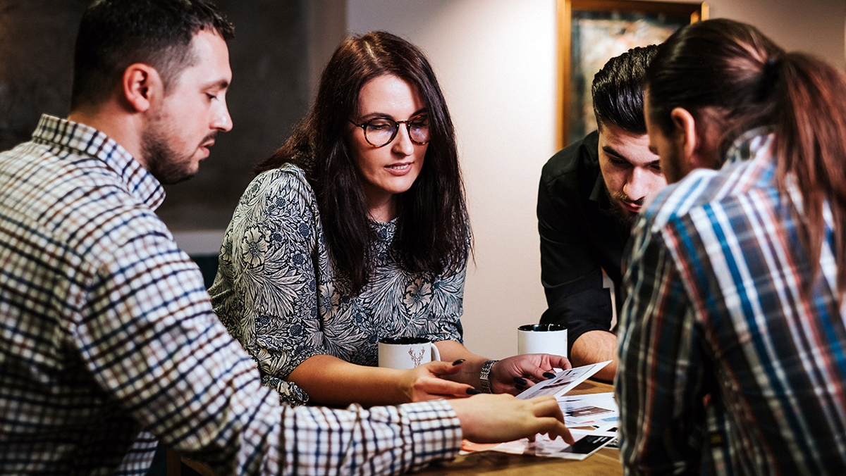Fyra personer runt ett bord med kaffemuggar och bilder som de tittar på.