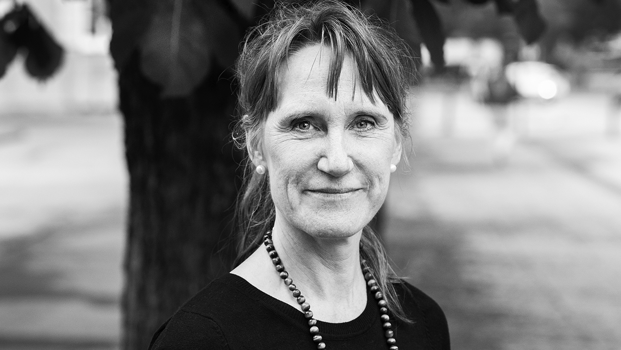 Person iförd halsband och mörk tröja stående framför träd.