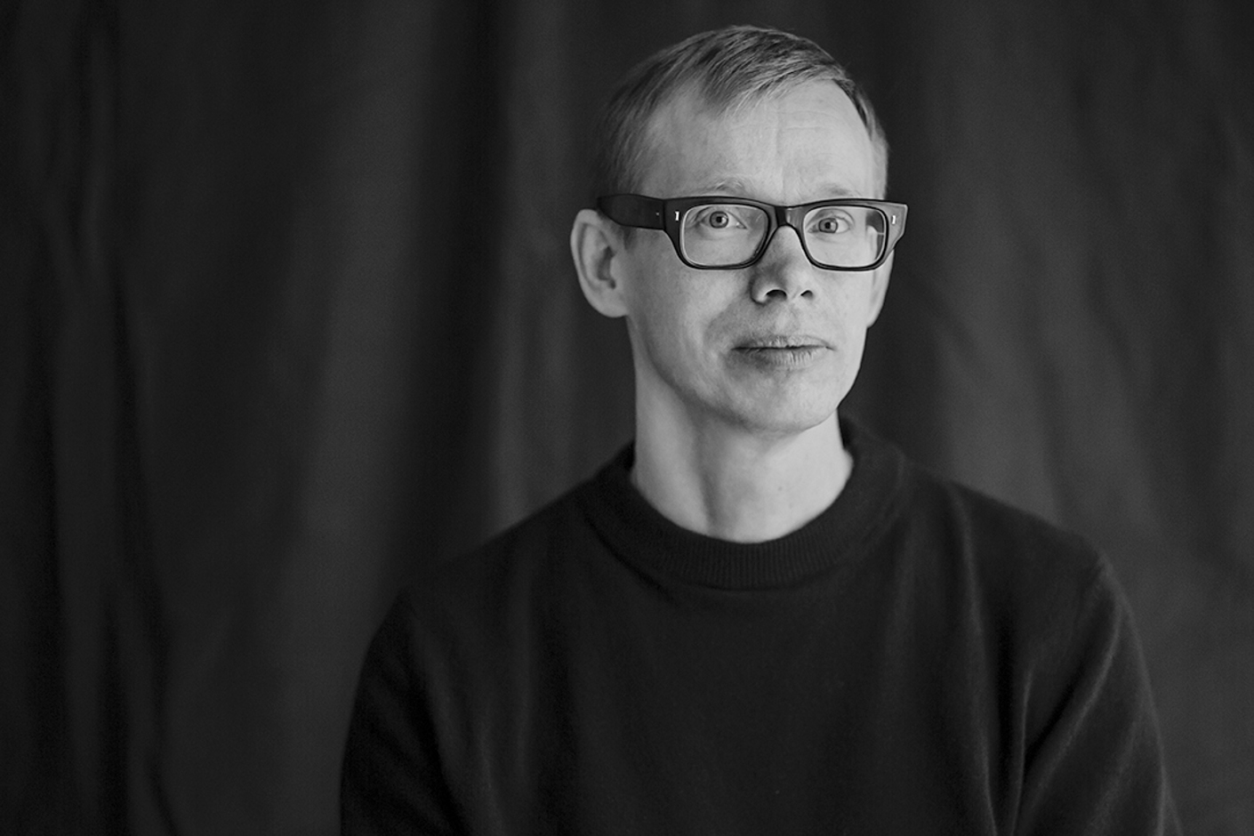 Person iförd svarta glasögon stående mot mörk bakgrund.