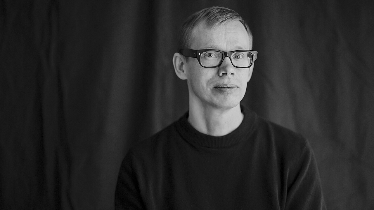 Person iförd svarta glasögon stående mot mörk bakgrund.