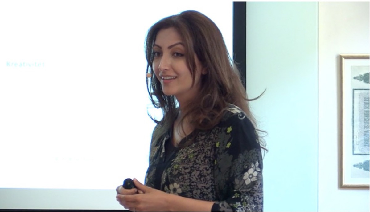 Person i föreläsarsituation iförd mönstrad blus.