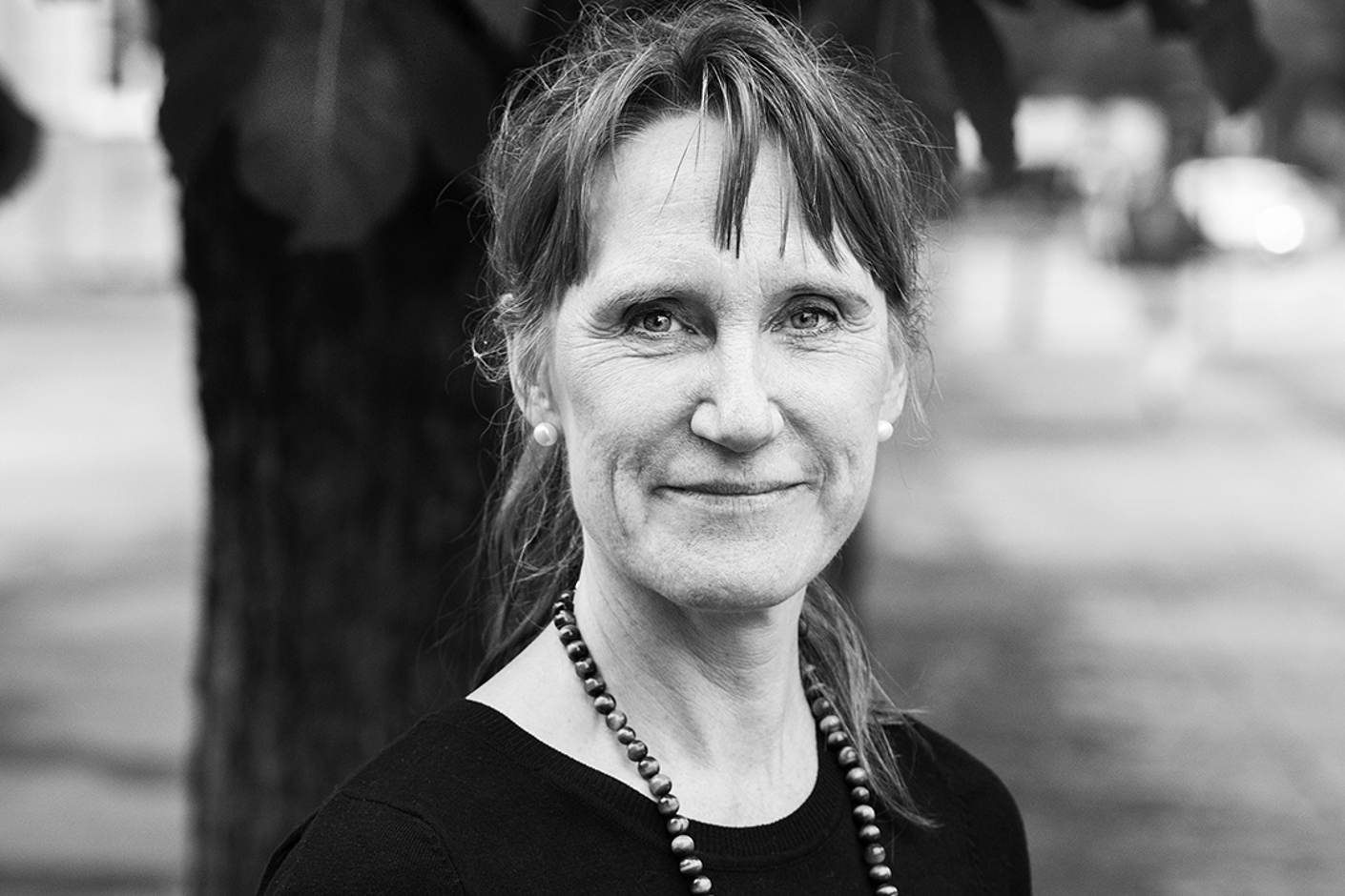 Person iförd halsband och mörk tröja stående framför träd.