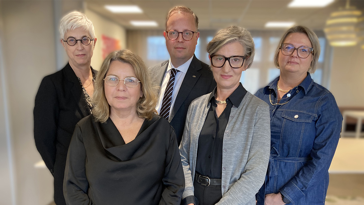 Fem personer står i kontorsmiljö och tittar mot kameran.