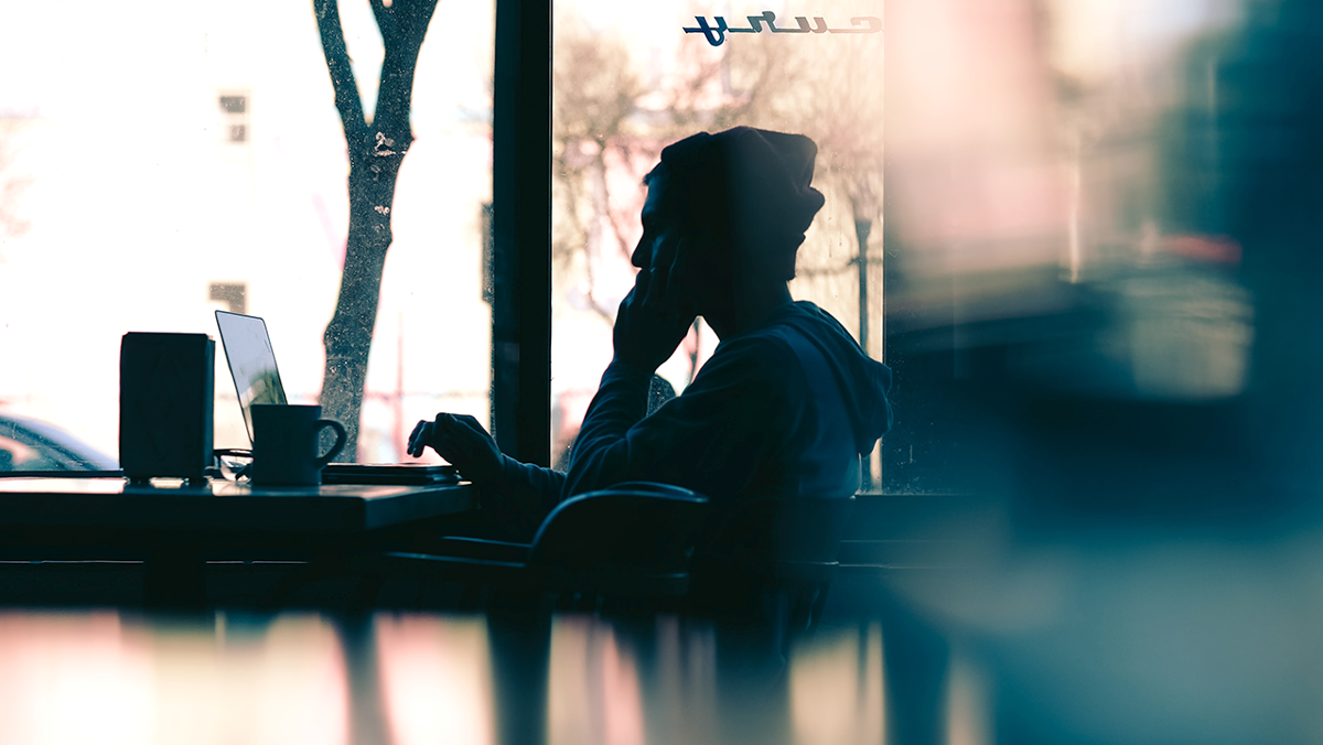 Person som sitter på café och jobbar med bärbara datorn framför sig.