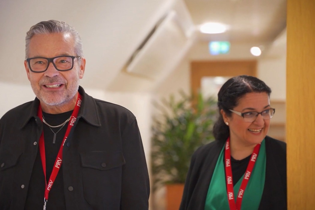 Två personer kommer gående i en korridor, de har nyckelband från PRV runt halsen. 