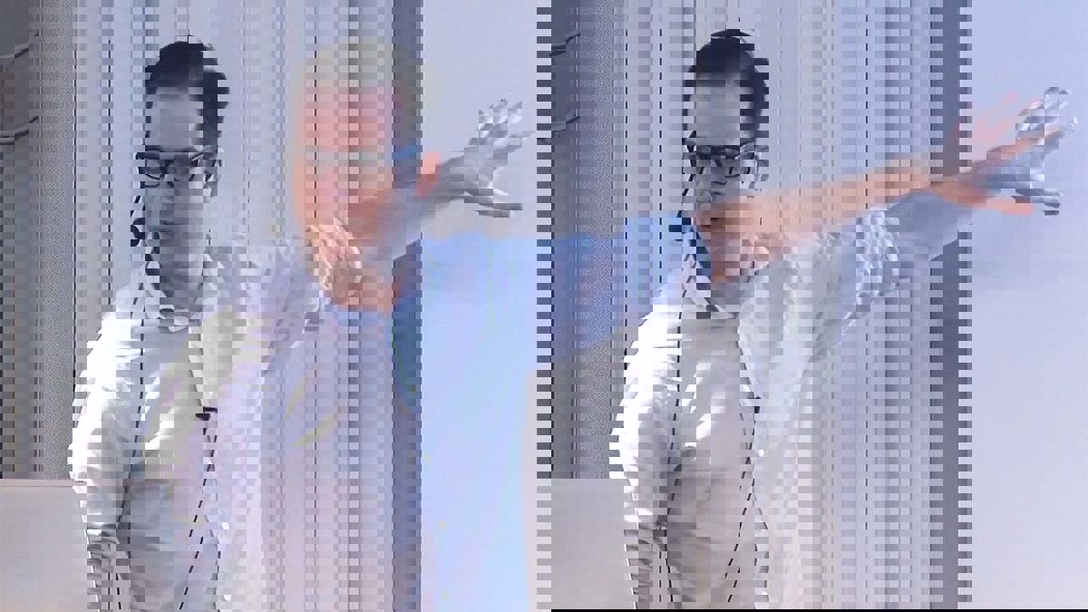 Person i föreläsningssituation iförd blå skjorta och mörkbågade glasögon.