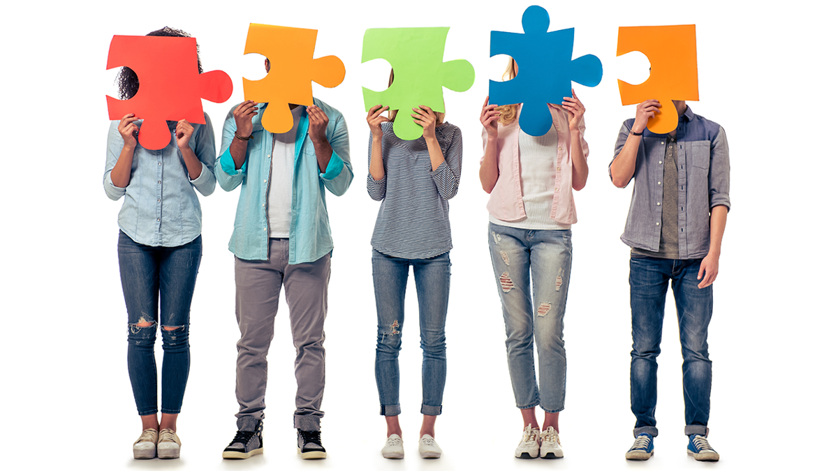 Fem personer står på led och håller upp stora, färgglada pusselbitar framför ansiktet.