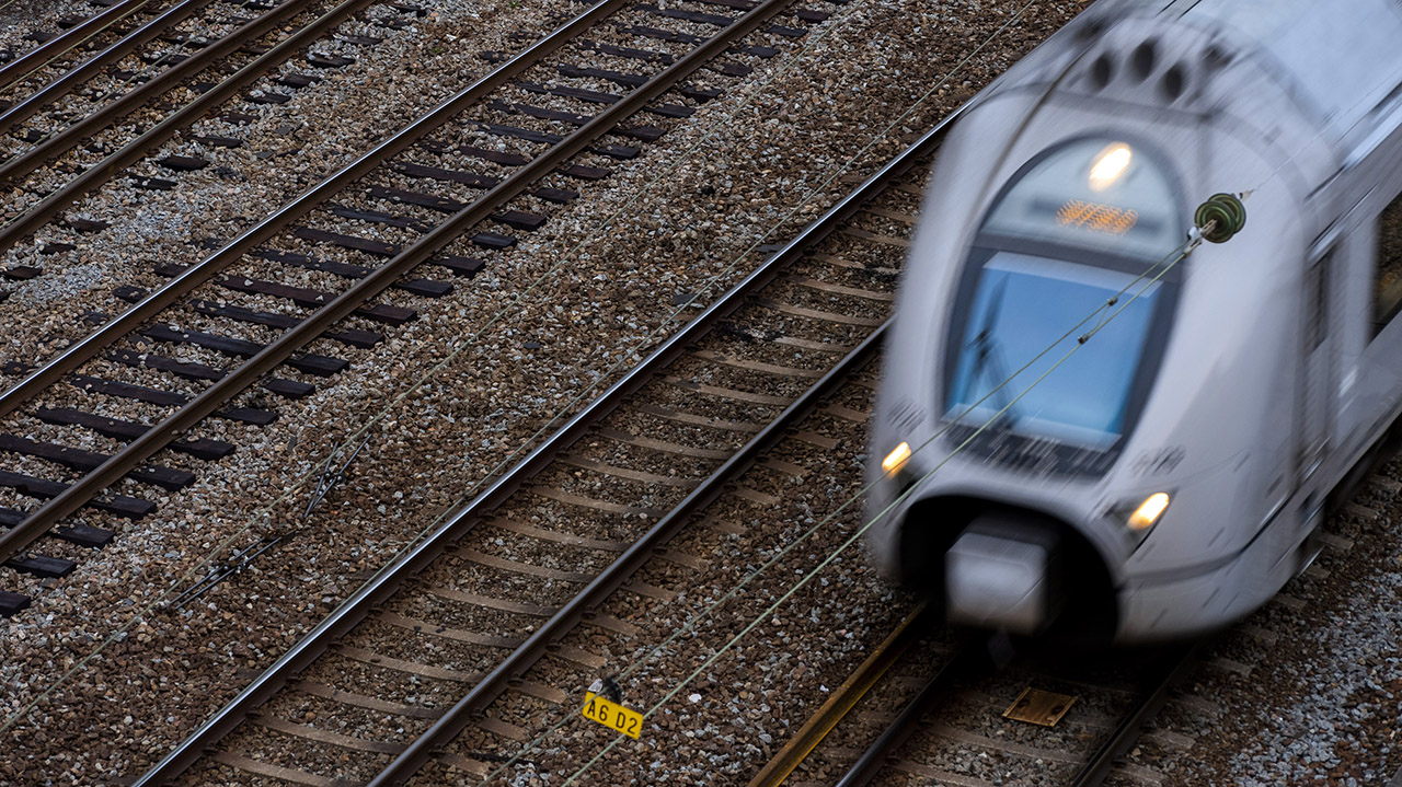 Bild föreställande tågspår och ett tåg som rör sig i snabb fart till höger i bild.