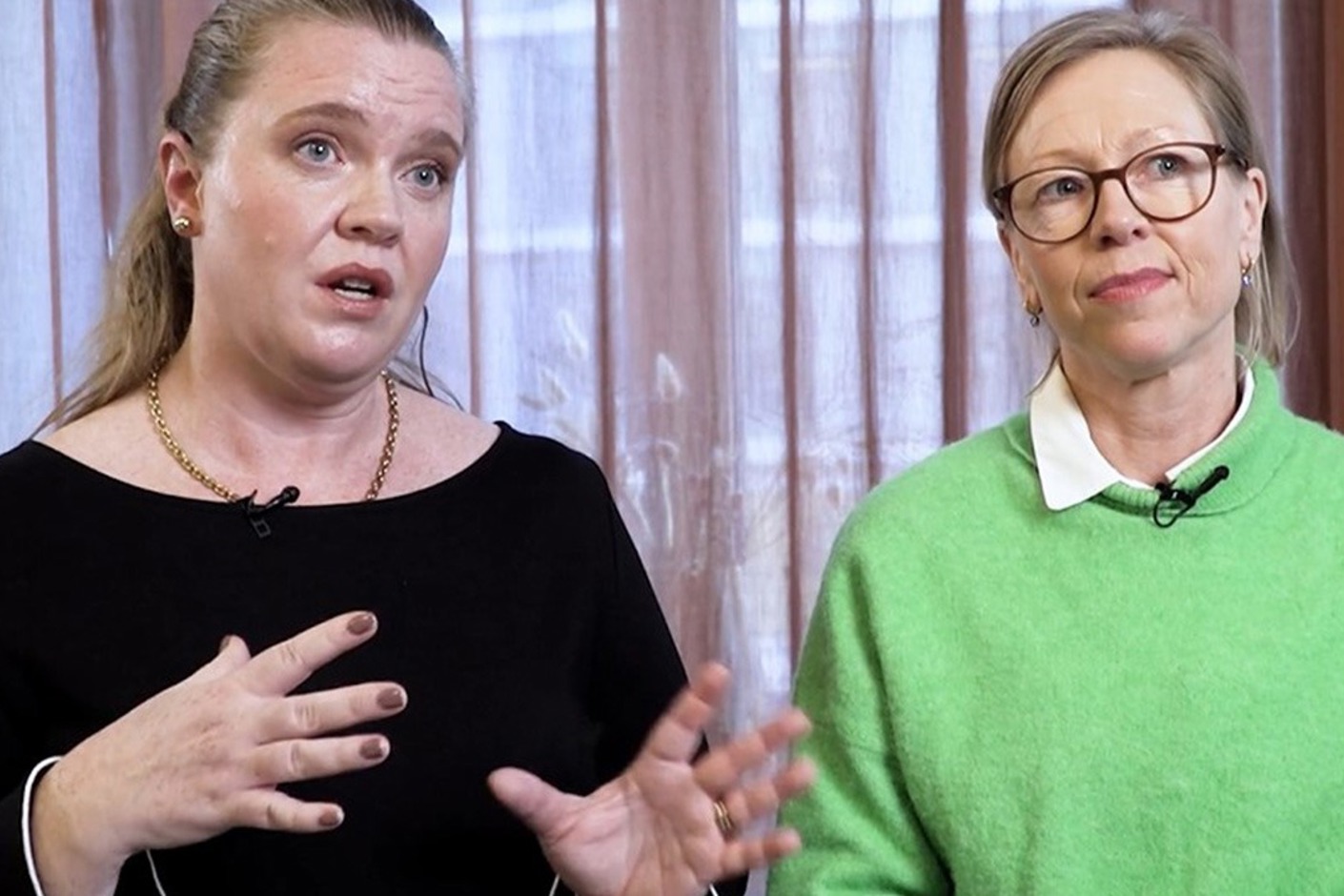 Två personer står framför ett fönster och samtalar in i kameran.