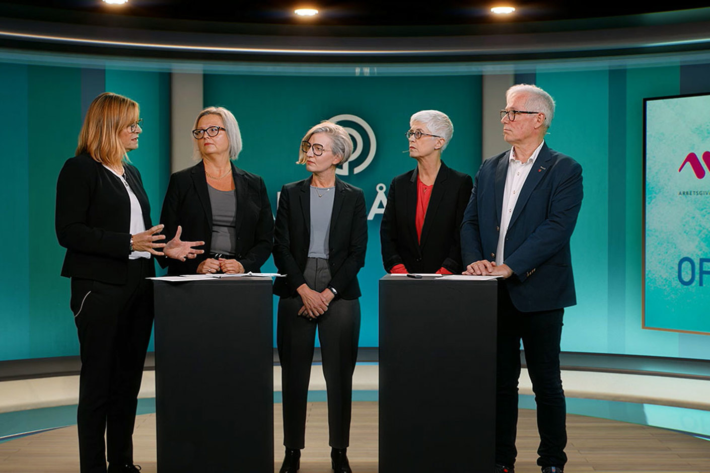 Fem personer samlade runt två svarta pulpeter i direktsändning.