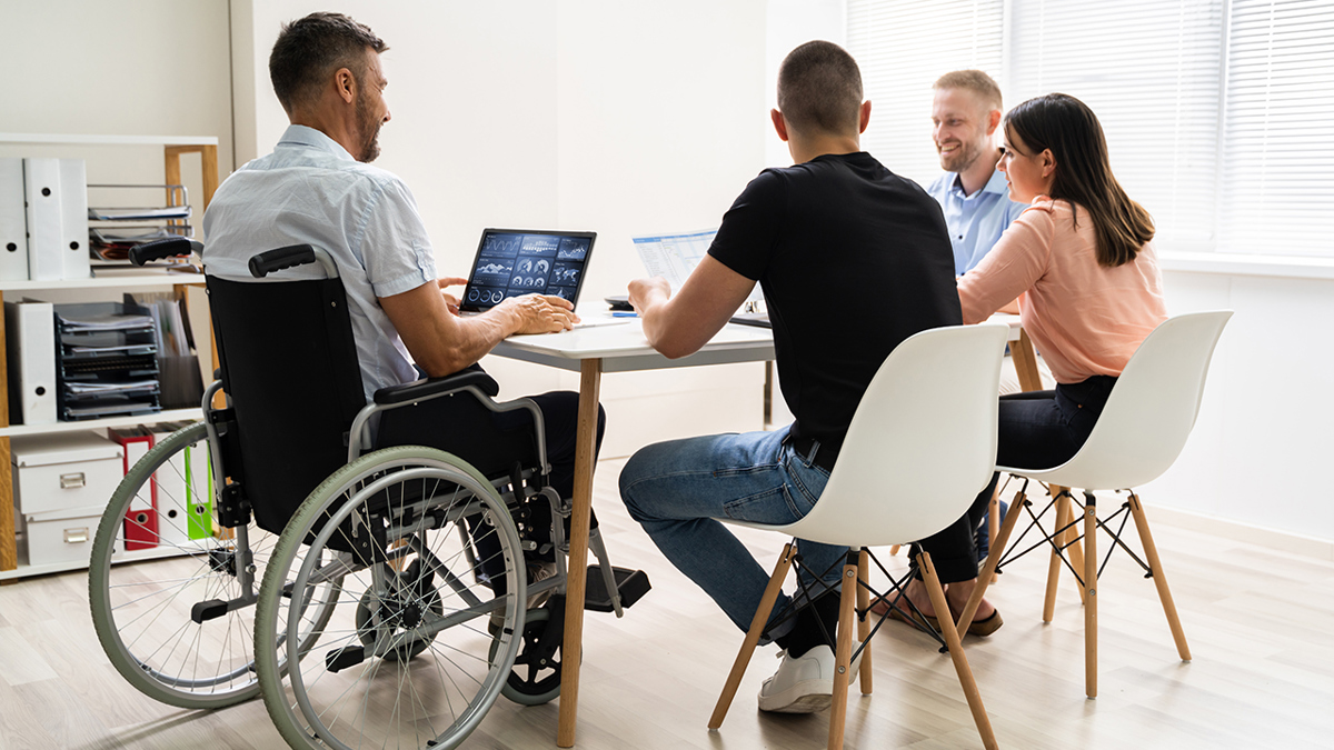 Mötessituation med fyra personer där den som håller i mötet sitter i rullstol.