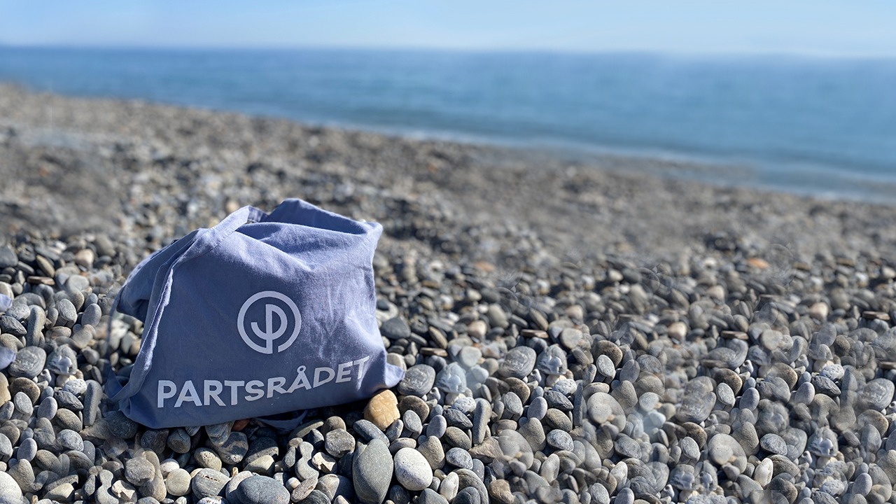 En blå tygpåse med Partsrådets logotyp som står på en stenstrand i Spanien.
