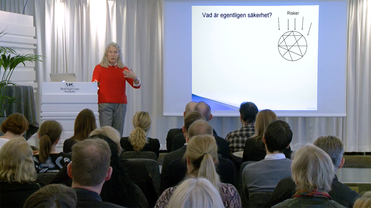 Person stående på scen framför åhörare.