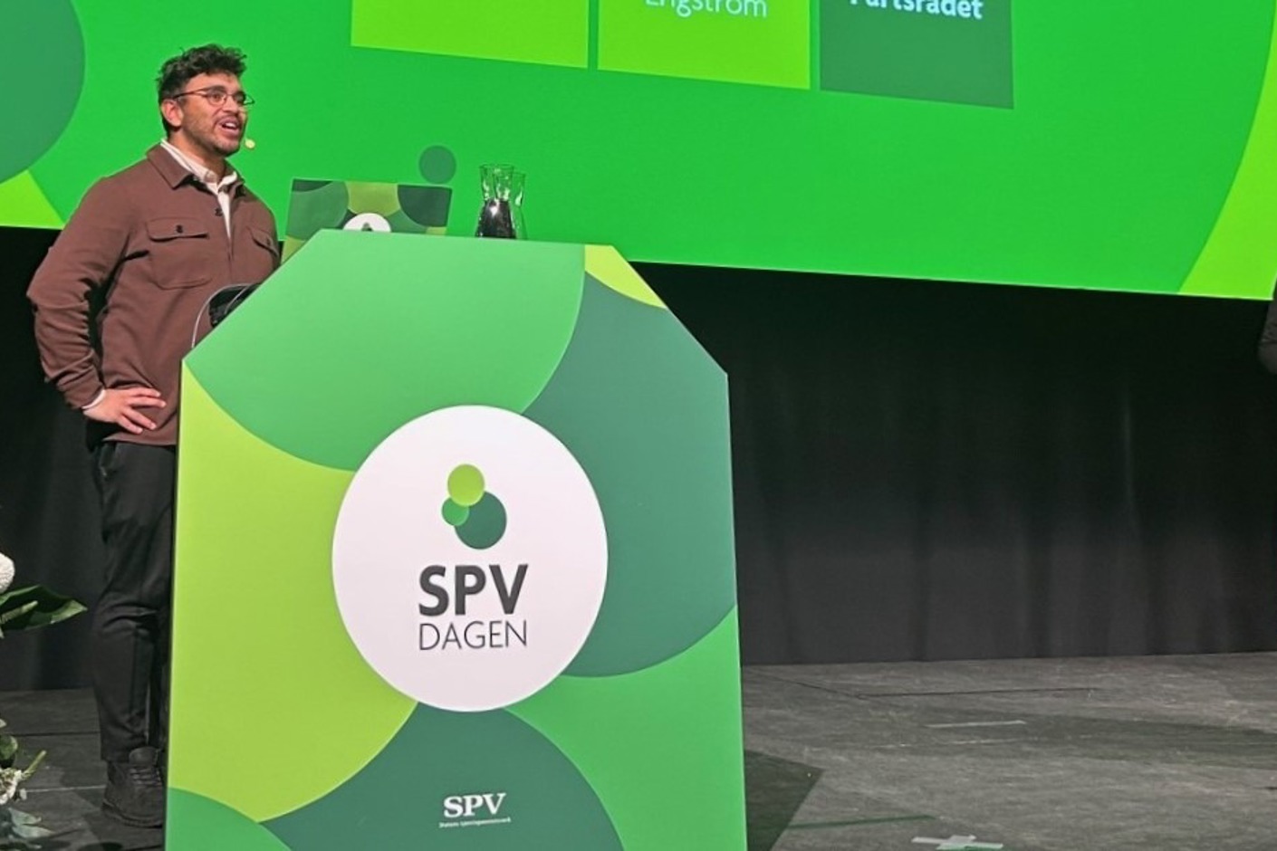 Två personer står på en scen. På talarstolen står det SPV-dagen.