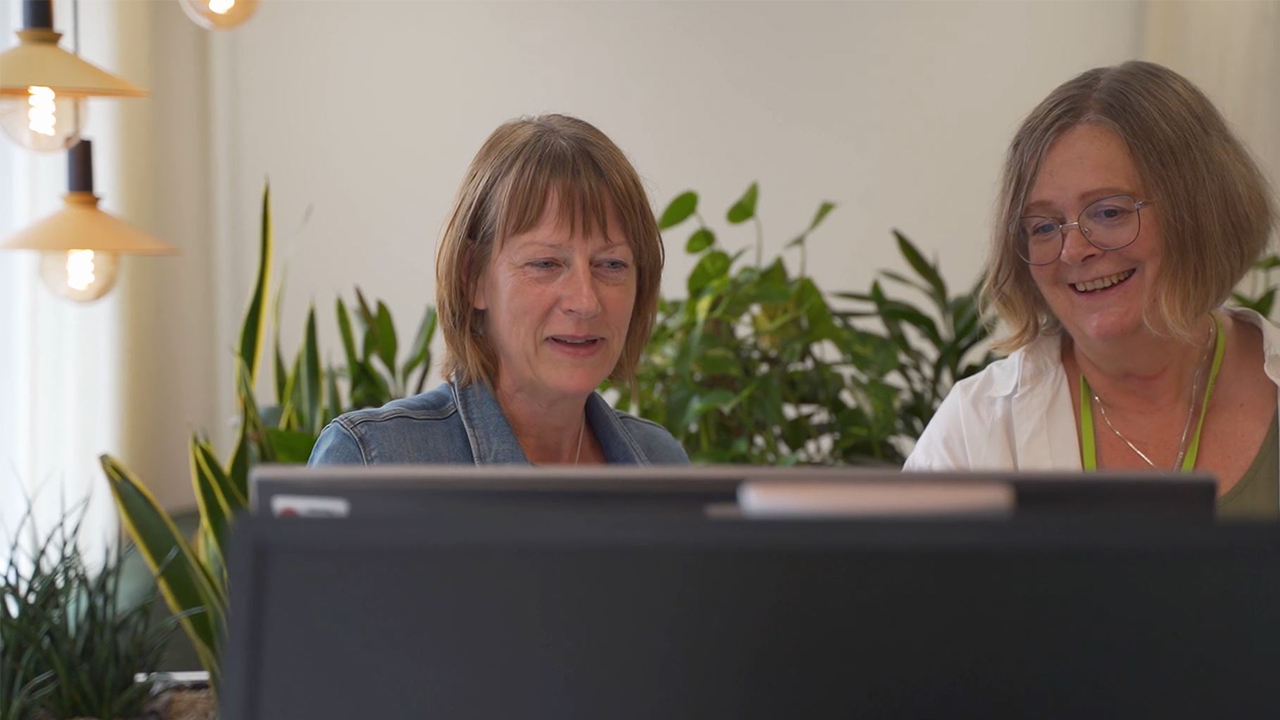 två personer står vid en dataskärm i ett kontorslandskap