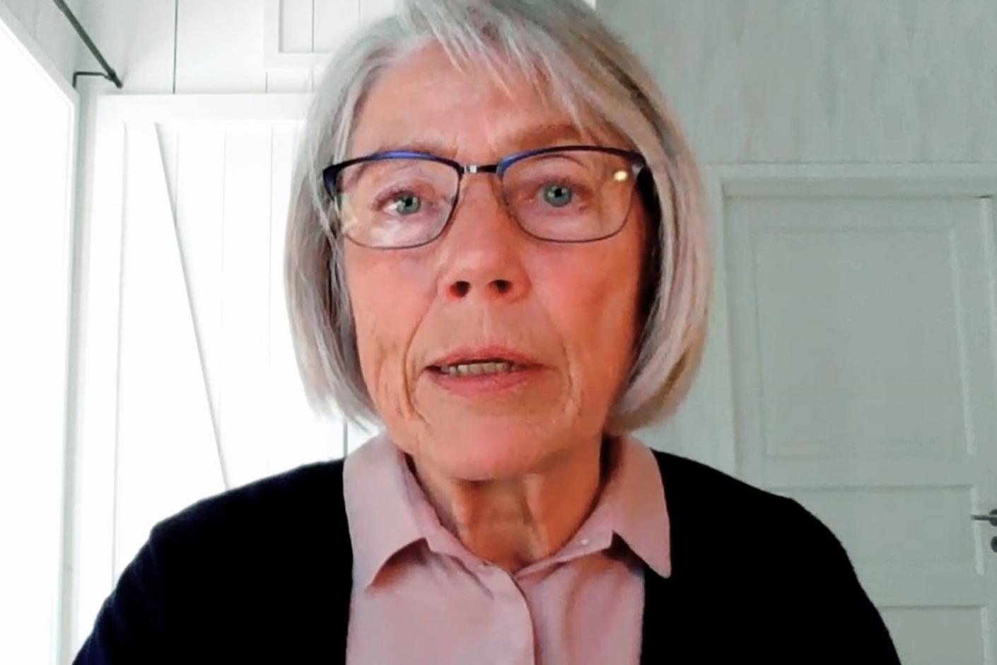 Huvudbild av person i hemmamiljö (vita väggar och dörrar) som blickar in i datorkameran.