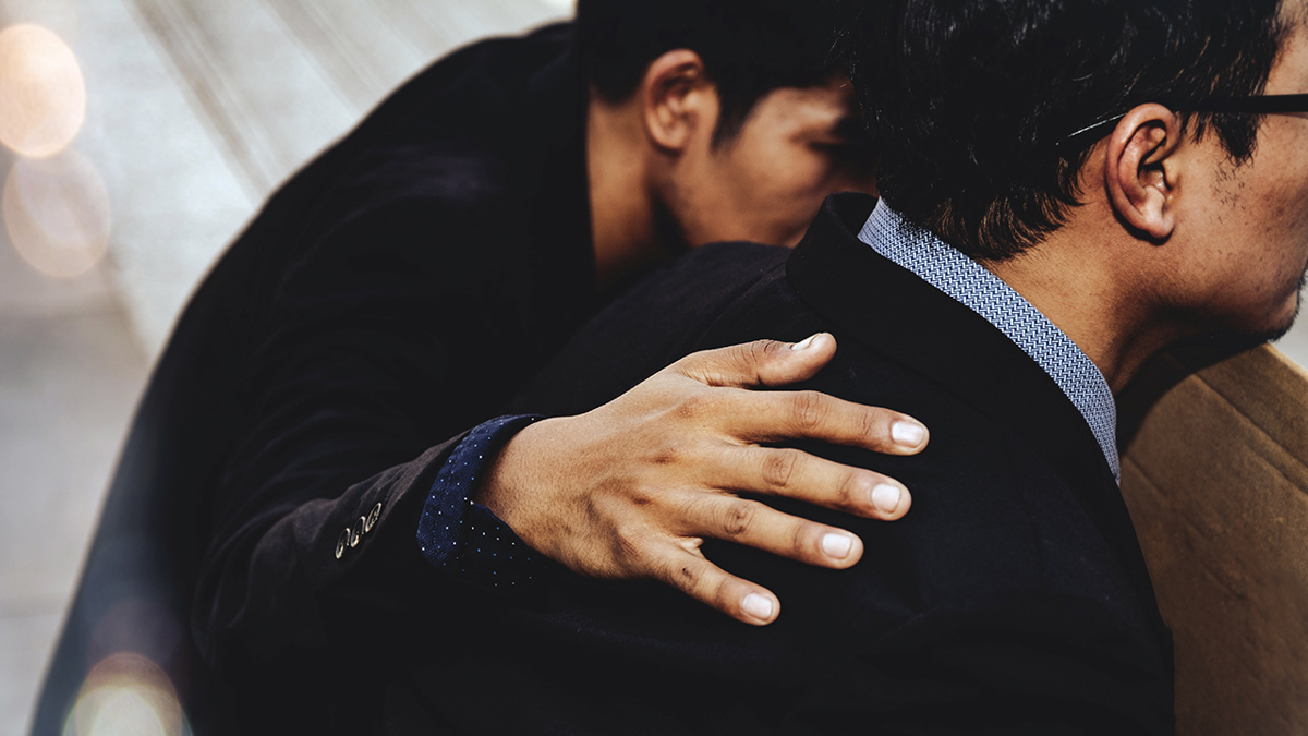 En person håller handen tröstande på en persons axel.