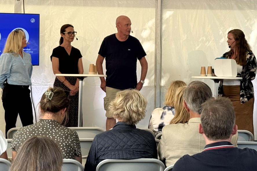 Fyra personer står i ett tält på ett seminarium. Publik sitter i förgrunden.