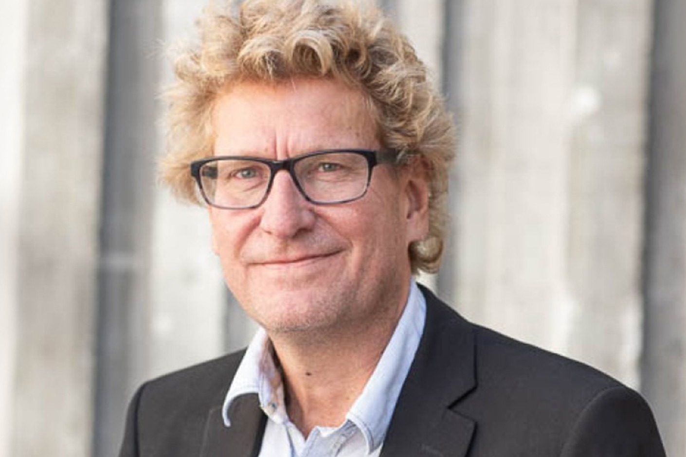 Person iförd mörkgrå kostym och skjorta, samt glasögon.