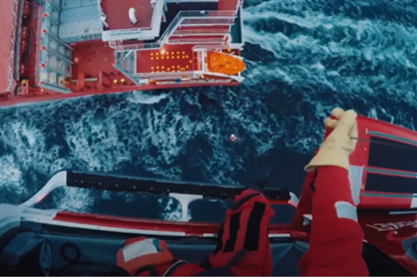 Ur perspektivet för en medarbetare som befinner sig på helikopter ser vi havet långt ner med en person i vattnet och ett lastfartyg bredvid.