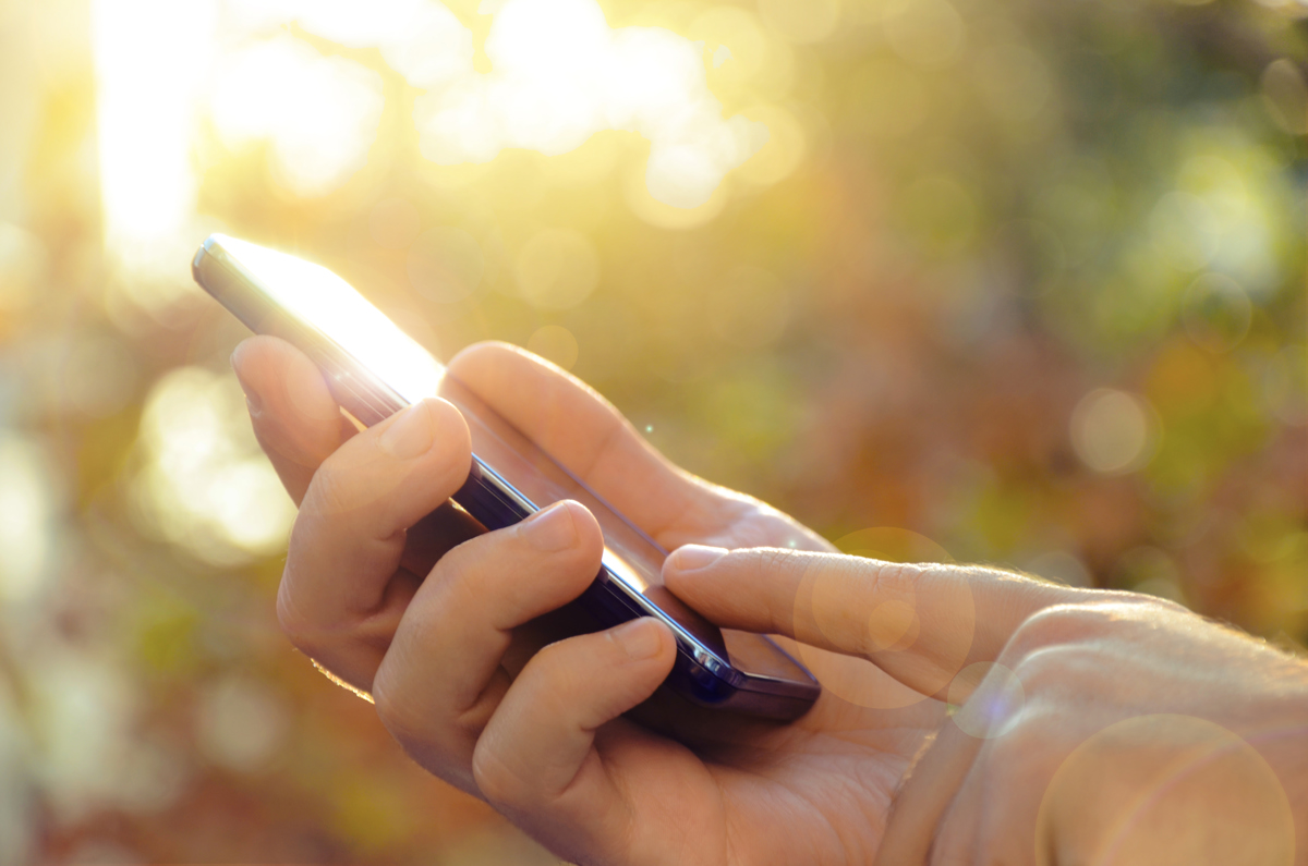 En mobiltelefon i handen mot en grön och belyst suddig naturbakgrund.