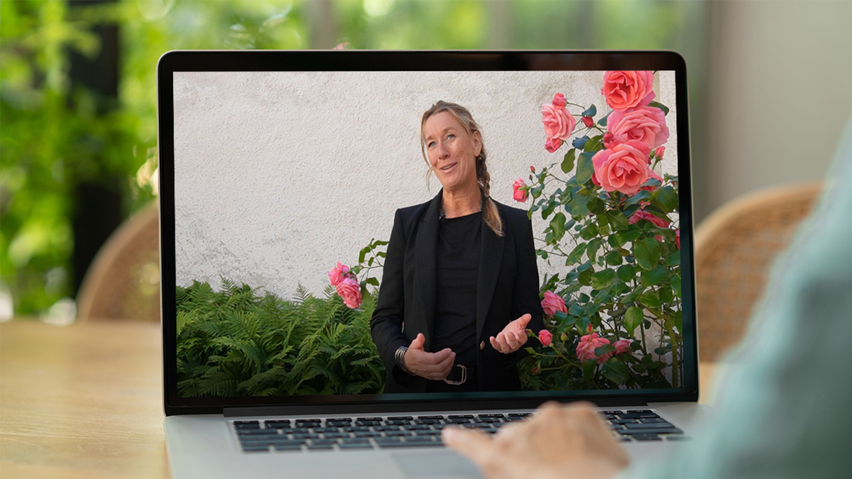 Person sitter vid dator och tittar på en kvinna som pratar.